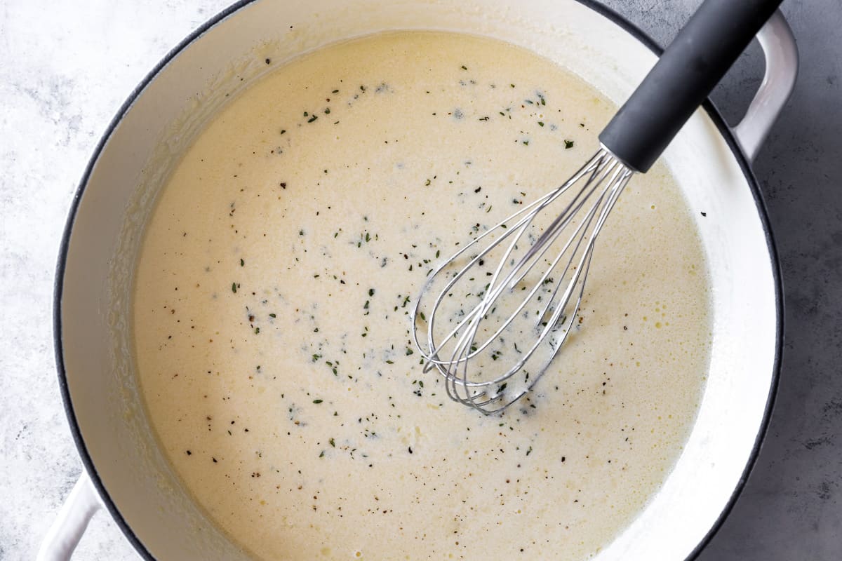 homemade alfredo sauce in a white dutch oven with a whisk.