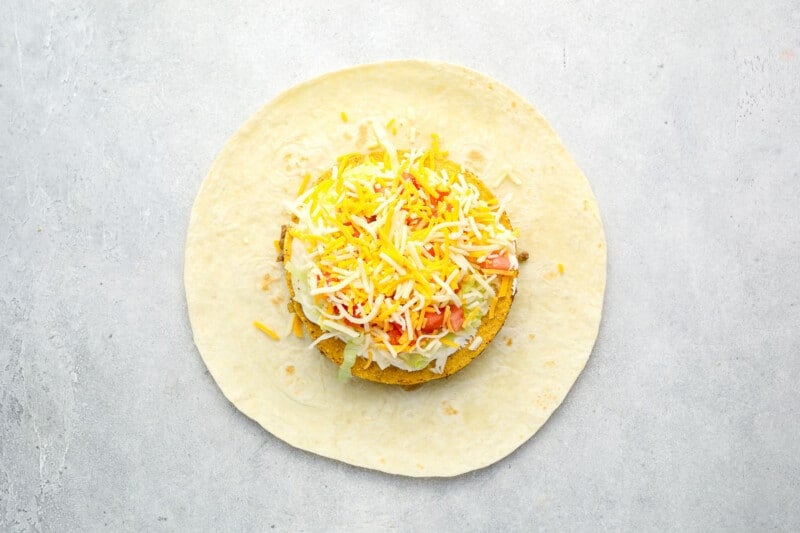sour cream, lettuce, tomatoes, and shredded cheese on a tostada over cheesy beef on a large flour tortilla.