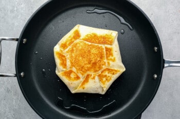 a partially cooked crunchwrap supreme flipped to show the seam side in a skillet.