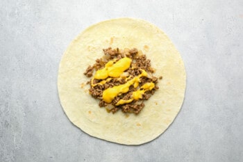nacho cheese sauce on top of ground beef on a large flour tortilla.