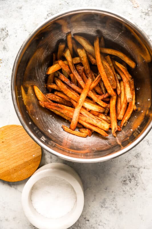 homemade french fries in a stainless steel bowl with salt.