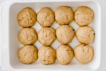 12 hot cross bun dough balls in a rectangular baking pan.