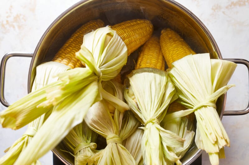 8 ears of corn pointed down into a deep pot of water with the husks pulled back and sticking up.