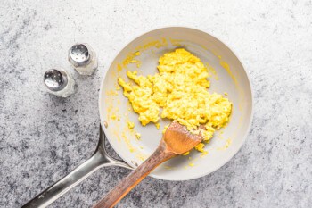overhead view of cooked scrambled eggs in a frying pan with a wooden spatula.