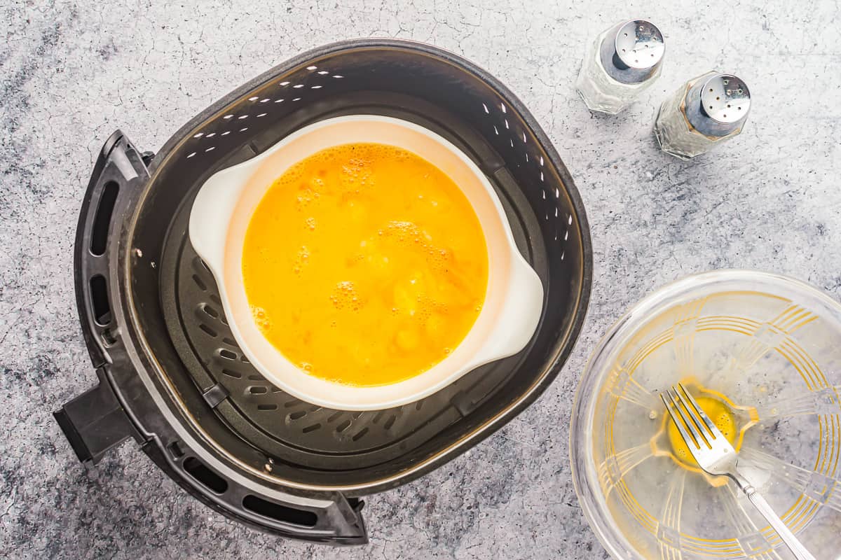 overhead view of raw eggs in a ramekin in an air fryer.