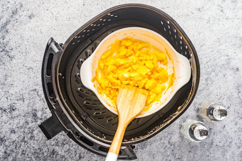 overhead view of scrambled eggs in a ramekin in an air fryer with a wooden spatula.