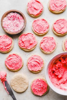 lofthouse sugar cookies being frosted with pink frosting and white and red sprinkles.