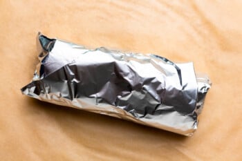 a make ahead breakfast burrito wrapped in foil on a wooden cutting board.