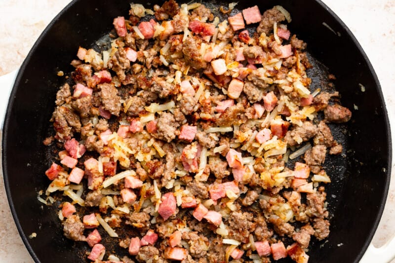 sausage, ham, and hashbrowns in a cast iron pan.