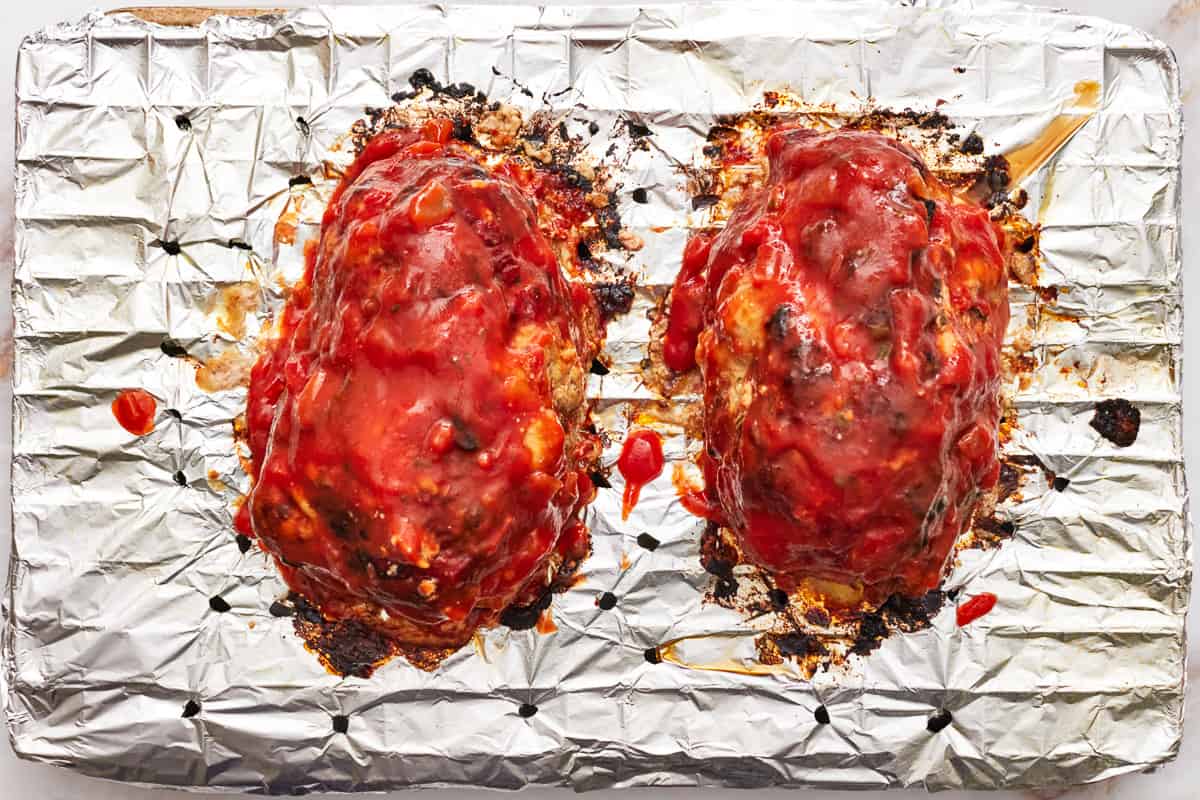 2 cooked mozzarella stuffed meatloaves covered in sauce on a wire rack. - 12
