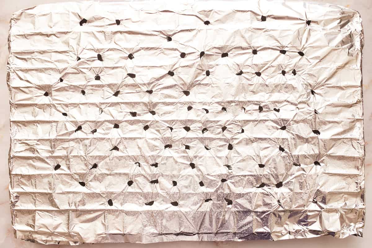 A wire rack covered in foil with holes poked into it over a baking sheet. - 6