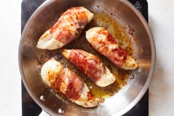 4 cooked prosciutto wrapped chicken breasts in a frying pan.