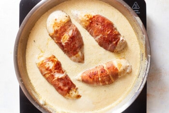 prosciutto wrapped chicken in sherry cream sauce in a frying pan.
