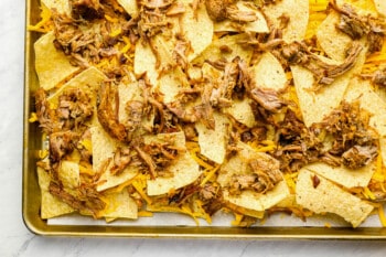 pork layered over tortilla chips, cheese, pork, and more tortilla chips on a baking sheet.