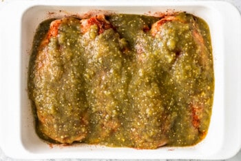 salsa verde poured over 4 chicken breasts in a rectangular baking pan.