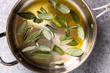 overhead view of sage leaves frying in oil in a skillet.