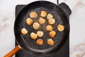 overhead view of seared scallops in a cast iron pan.