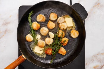 overhead view of seared scallops in a cast iron pan with butter and herbs.