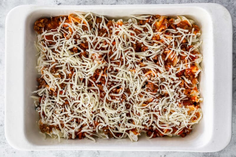 cheese on top of beef and noodle layers in a rectangular casserole dish.