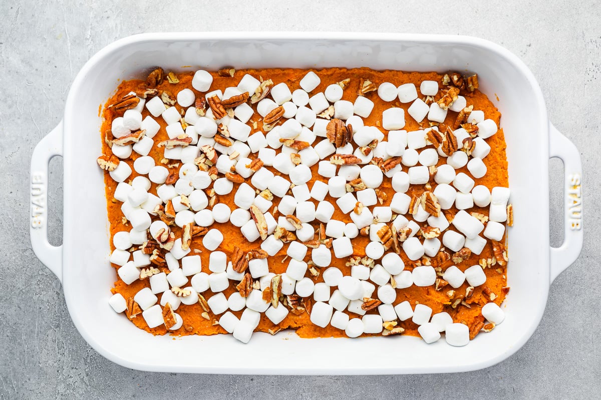 unbaked sweet potato casserole topped with mini marshmallows and pecans in a white rectangular casserole dish.
