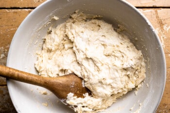 no knead focaccia dough in a white bowl with a wooden spoon.