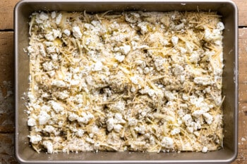 cheeses and herbs drizzled over no knead focaccia bread dough in a rectangular baking pan.
