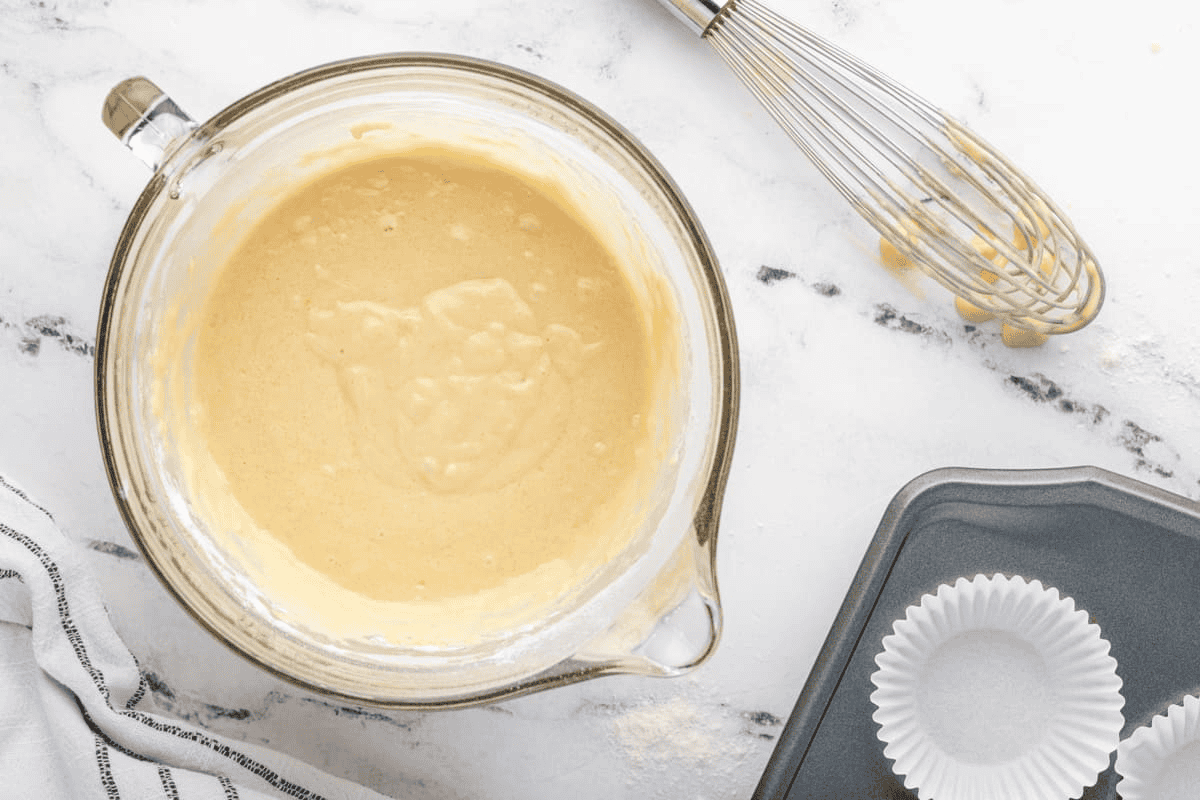Muffin batter in a large measuring cup with a whisk and a lined muffin tray.