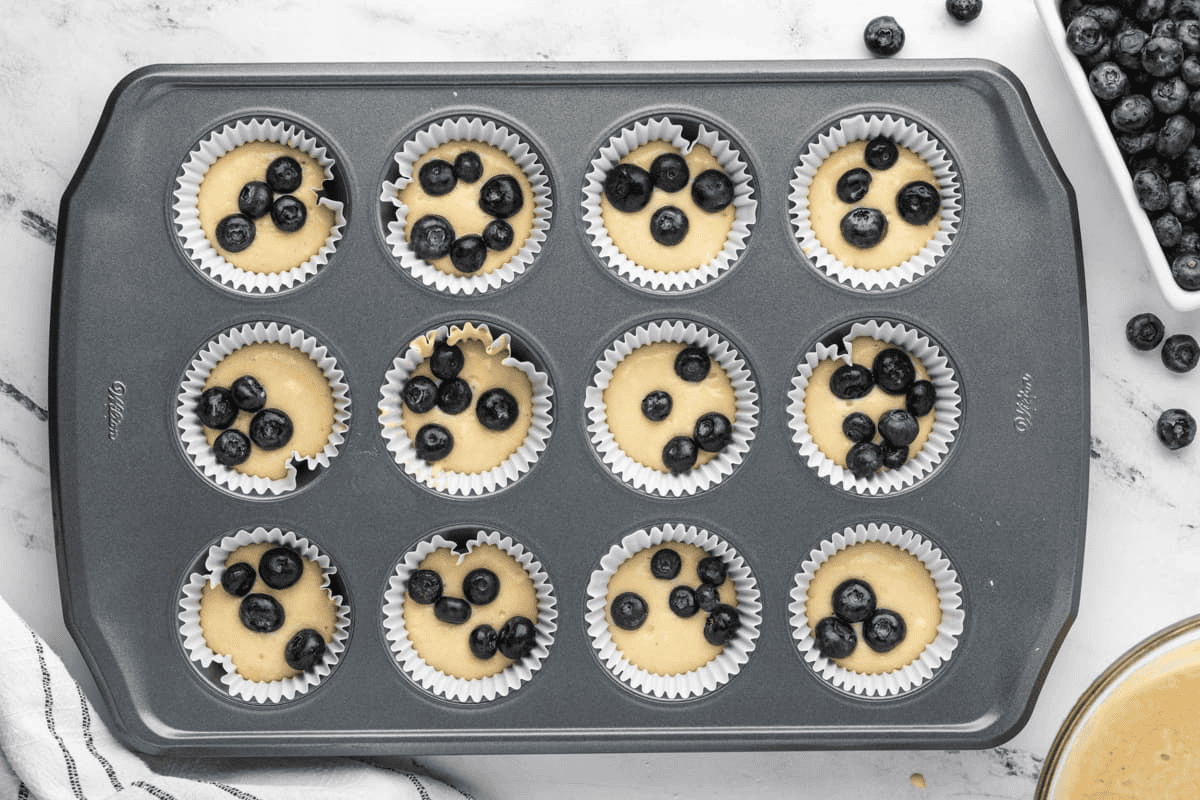 Placing blueberries on top of the batter in the muffin tray.