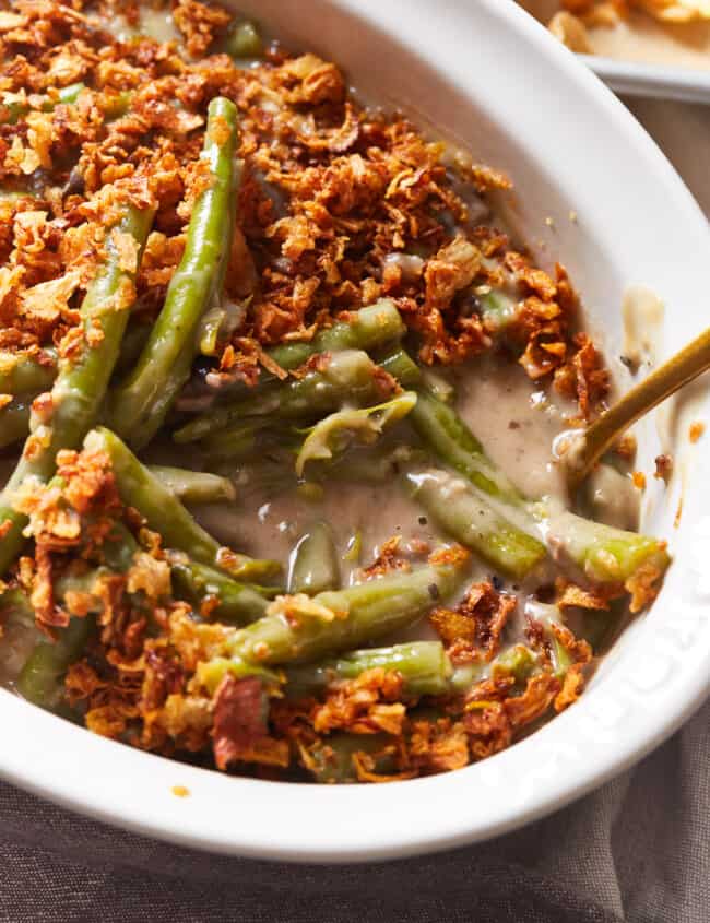 close up view of instant pot green bean casserole in a white serving dish with a spoon.