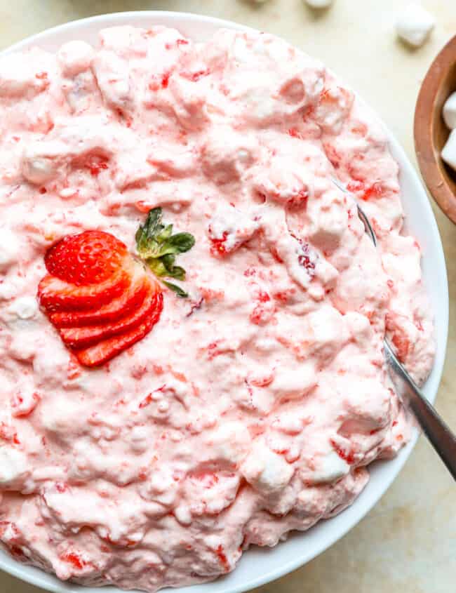 jello salad in a white bowl with a fanned out sliced strawberry on top and a spoon.