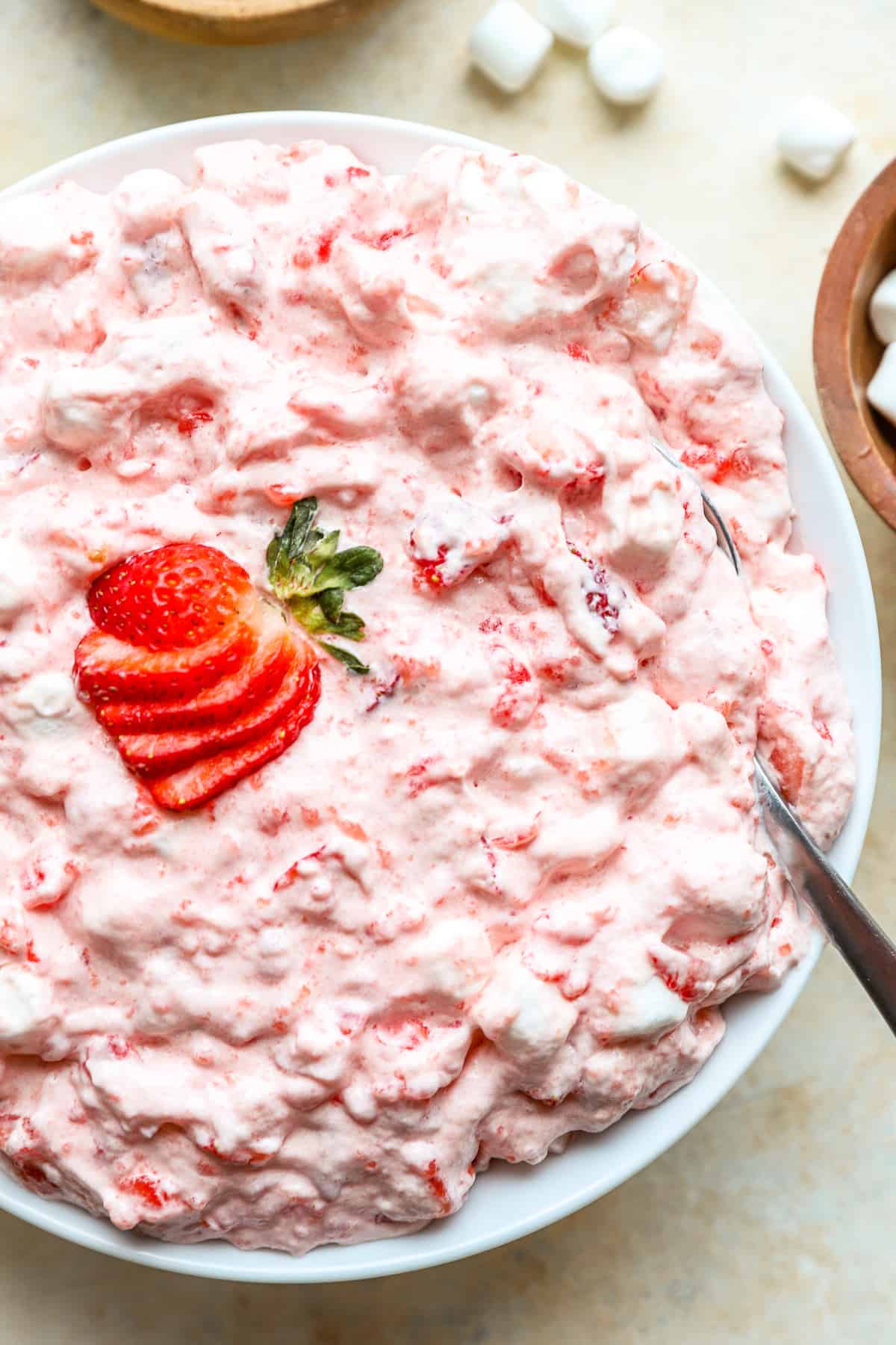 pink jello salad in a white bowl with a fanned out sliced strawberry on top and a spoon.