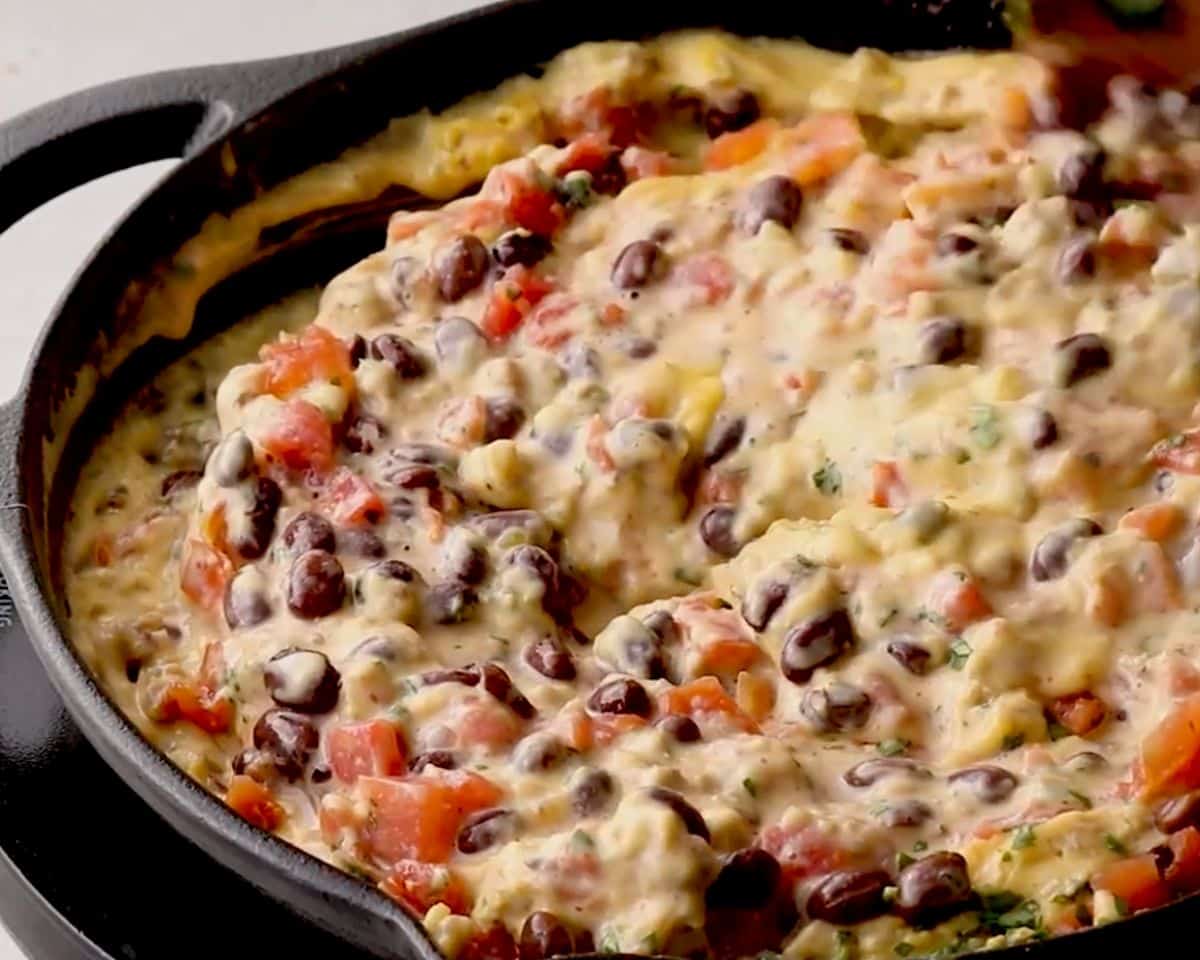 Loaded cowboy queso with black beans, diced tomatoes, and melted cheese in a cast iron skillet