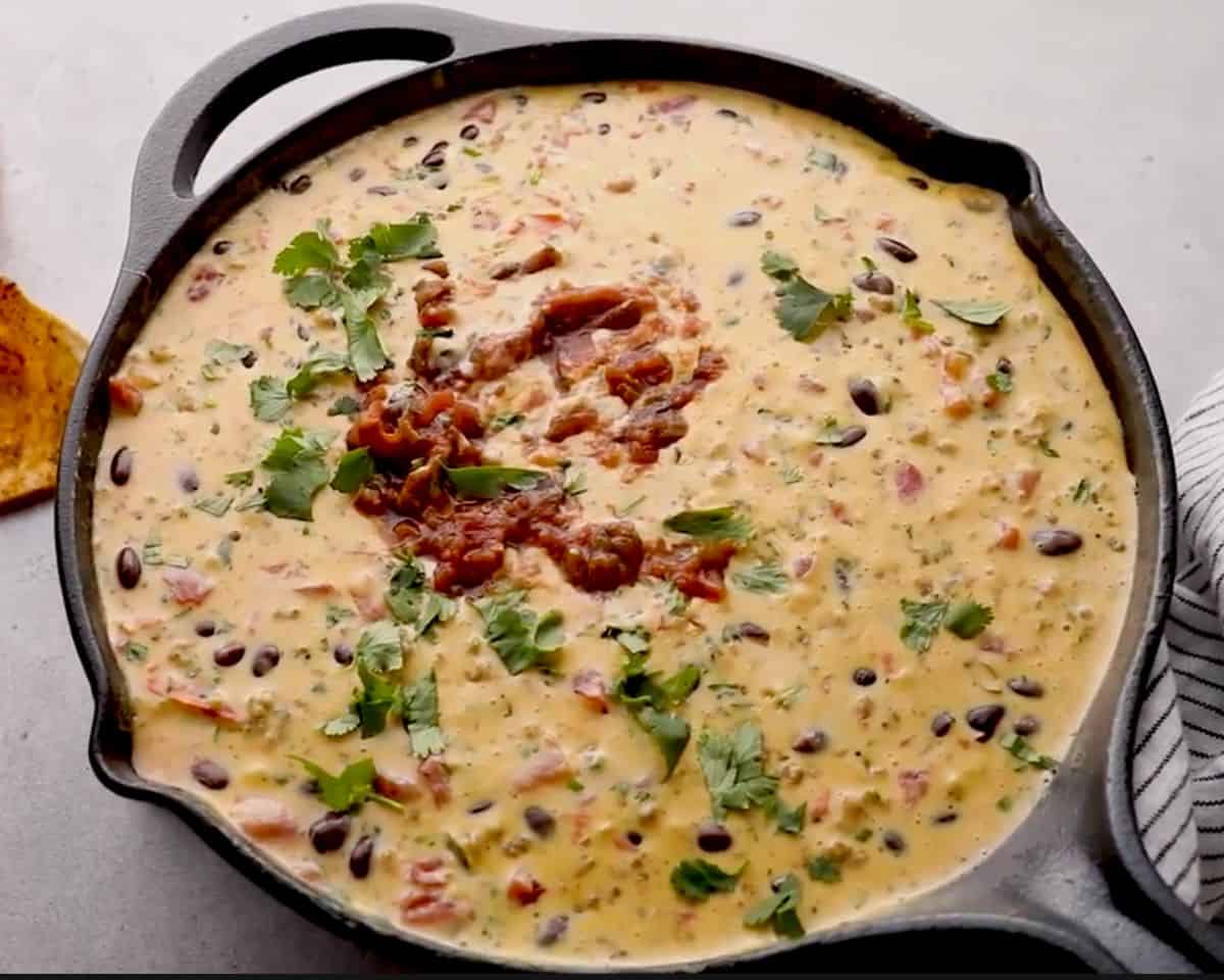 Finished loaded cowboy queso topped with cilantro in a skillet, ready to serve with tortilla chips