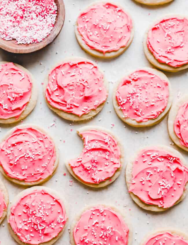 overhead view of pink frosted lofthouse cookies on parchment, one is bitten.