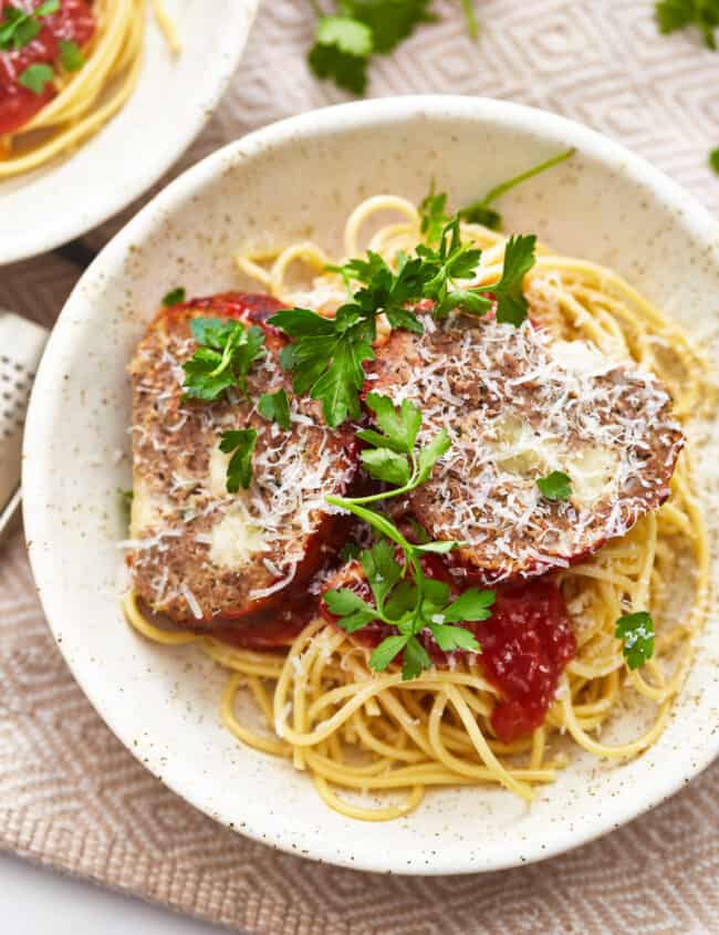 overhead view of slices of mozzarella stuffed meatloaf on a bed of pasta in a white bowl.