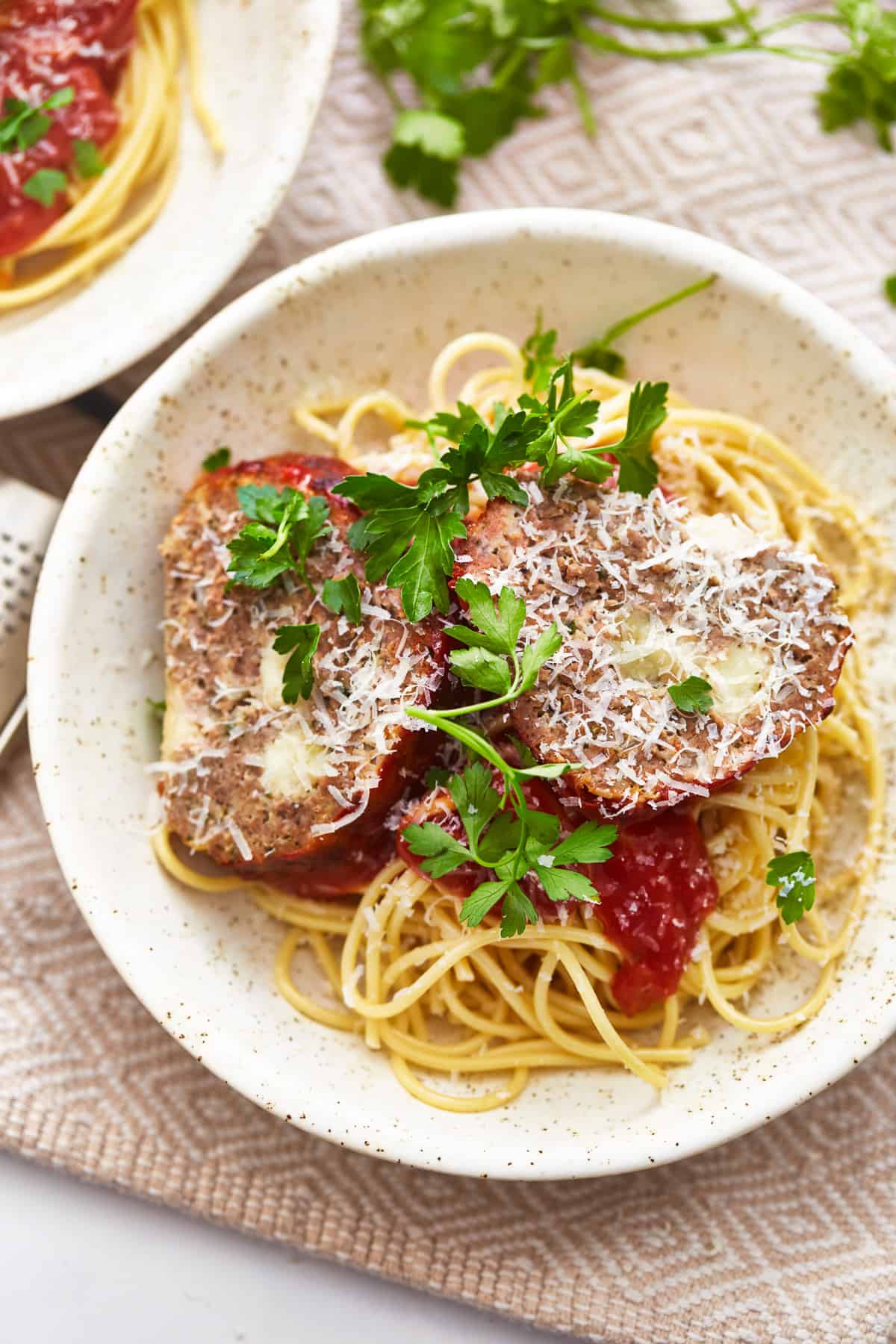 overhead view of slices of mozzarella stuffed meatloaf on a bed of pasta in a white bowl.