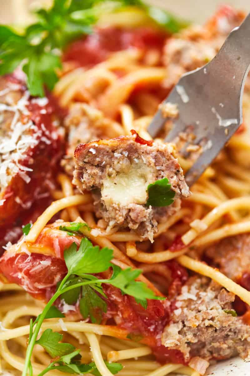 close up of a fork stabbing a piece of mozzarella stuffed meatloaf on a bed of pasta.