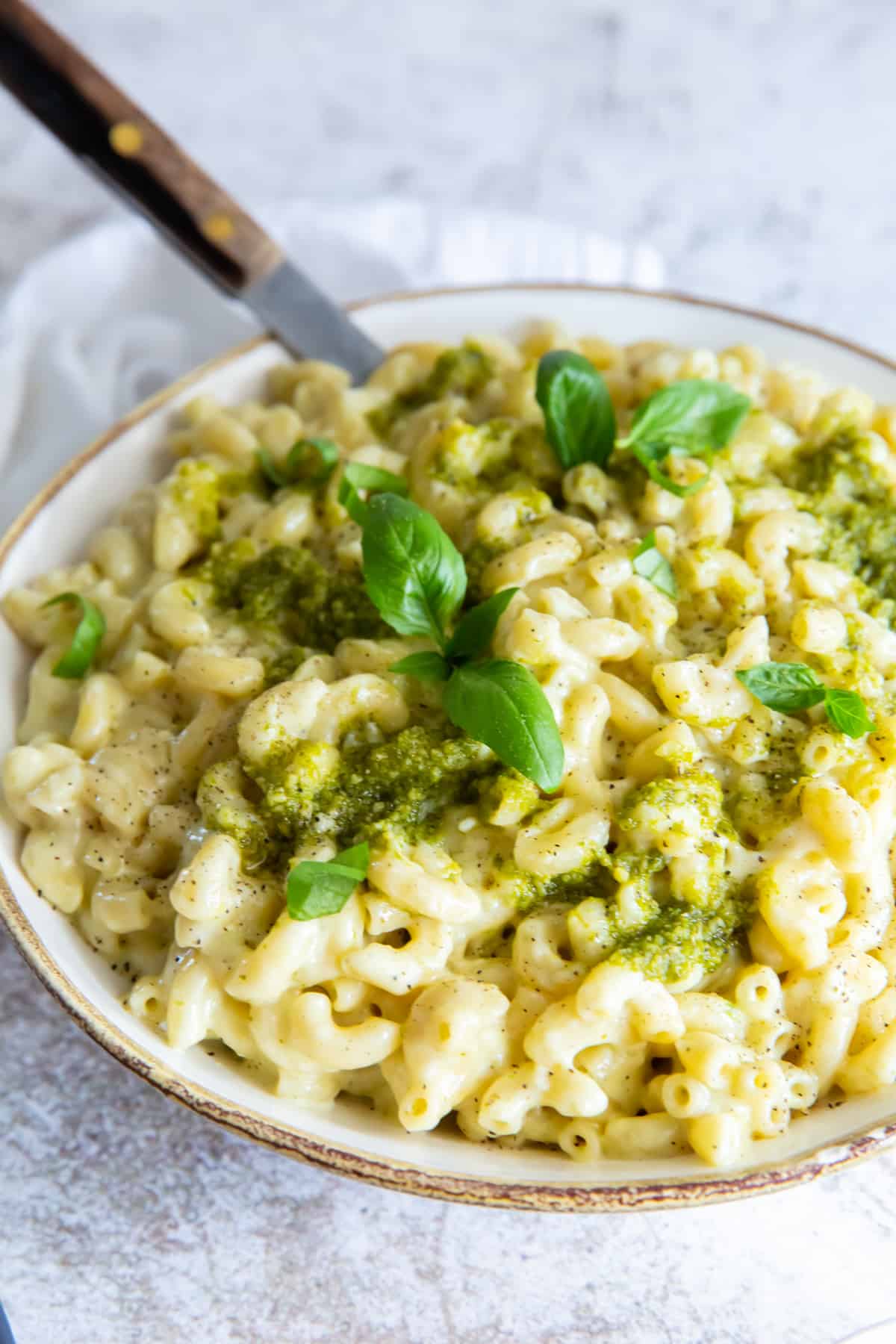 three-quarters view of a bowl of pesto mac and cheese with a fork.