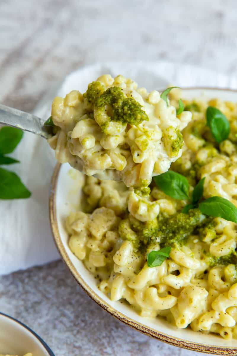 a forkful of pesto mac and cheese suspended in front of a bowl of pesto mac and cheese.
