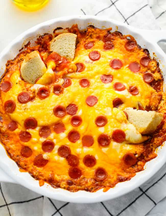 three-quarters view of pizza dip in a white round baking dish with 3 cubes of bread dipped in it.