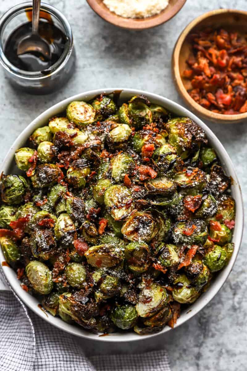 overhead view of roasted brussels sprouts topped with bacon, cheese, and balsamic in a serving bowl.