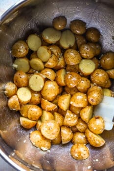 overhead view of halved baby potatoes tossed in oil and seasonings in a stainless bowl.