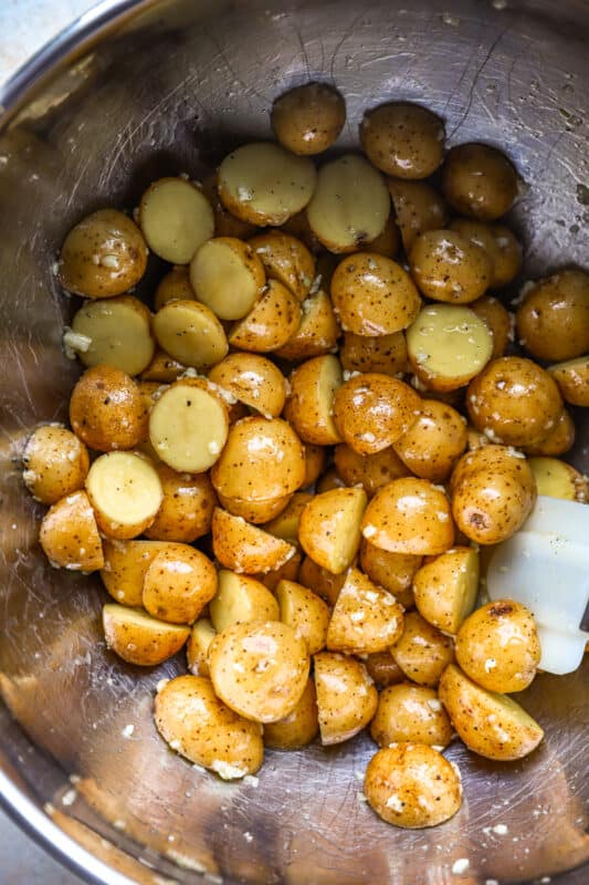 overhead view of halved baby potatoes tossed in oil and seasonings in a stainless bowl.