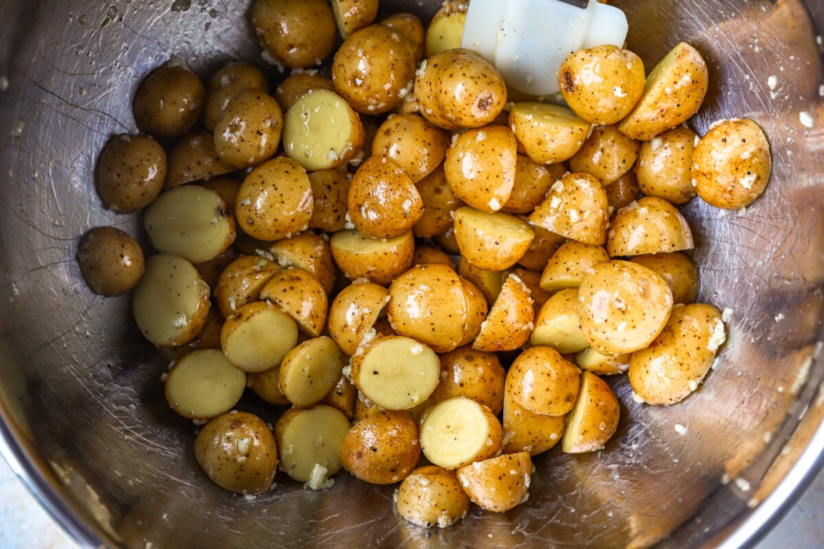 overhead view of halved baby potatoes tossed in oil and seasonings in a stainless bowl.