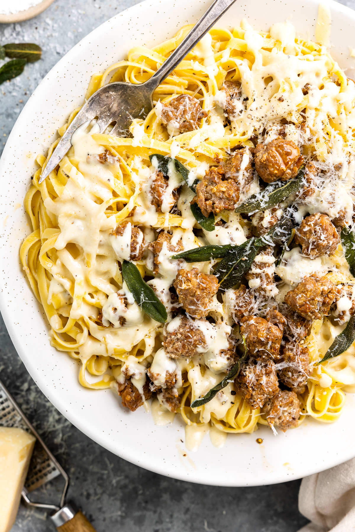 This SAUSAGE ALFREDO recipe is a tasty mix of classic Fettuccine Alfredo and spicy Italian Sausage. A lot of fettuccine recipes feature chicken or seafood, but there just aren't enough Sausage Pasta Recipes out there. This Italian Sausage Pasta recipe is the perfect pasta dish for your next dinner! partial overhead view of fettuccini alfredo on a white plate.
