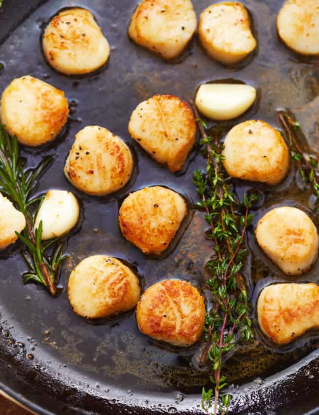 overhead view of seared scallops in a cast iron pan with herbs.