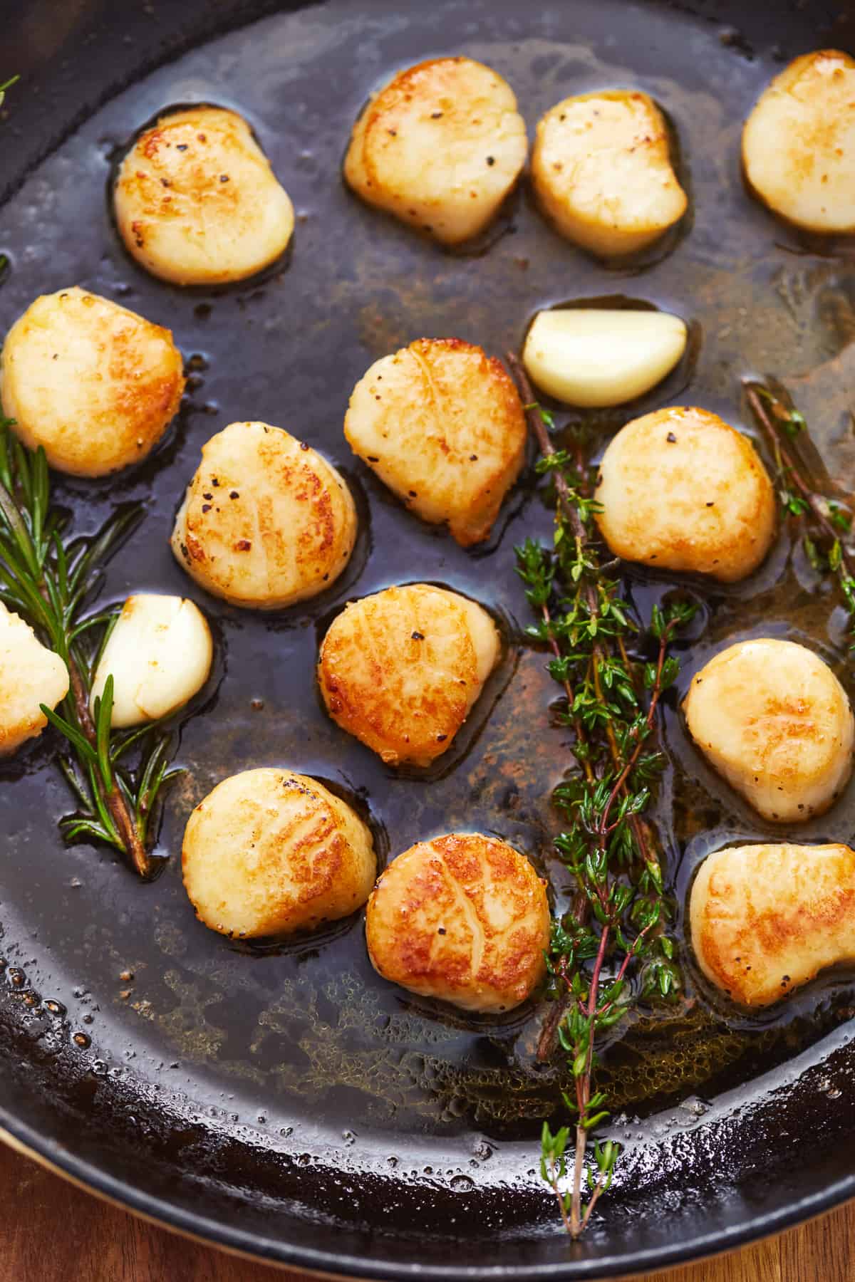 overhead view of seared scallops in a cast iron pan with herbs.