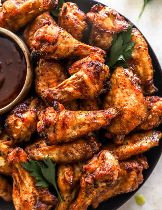 overhead view of smoked chicken wings on a black serving plate with barbecue sauce.