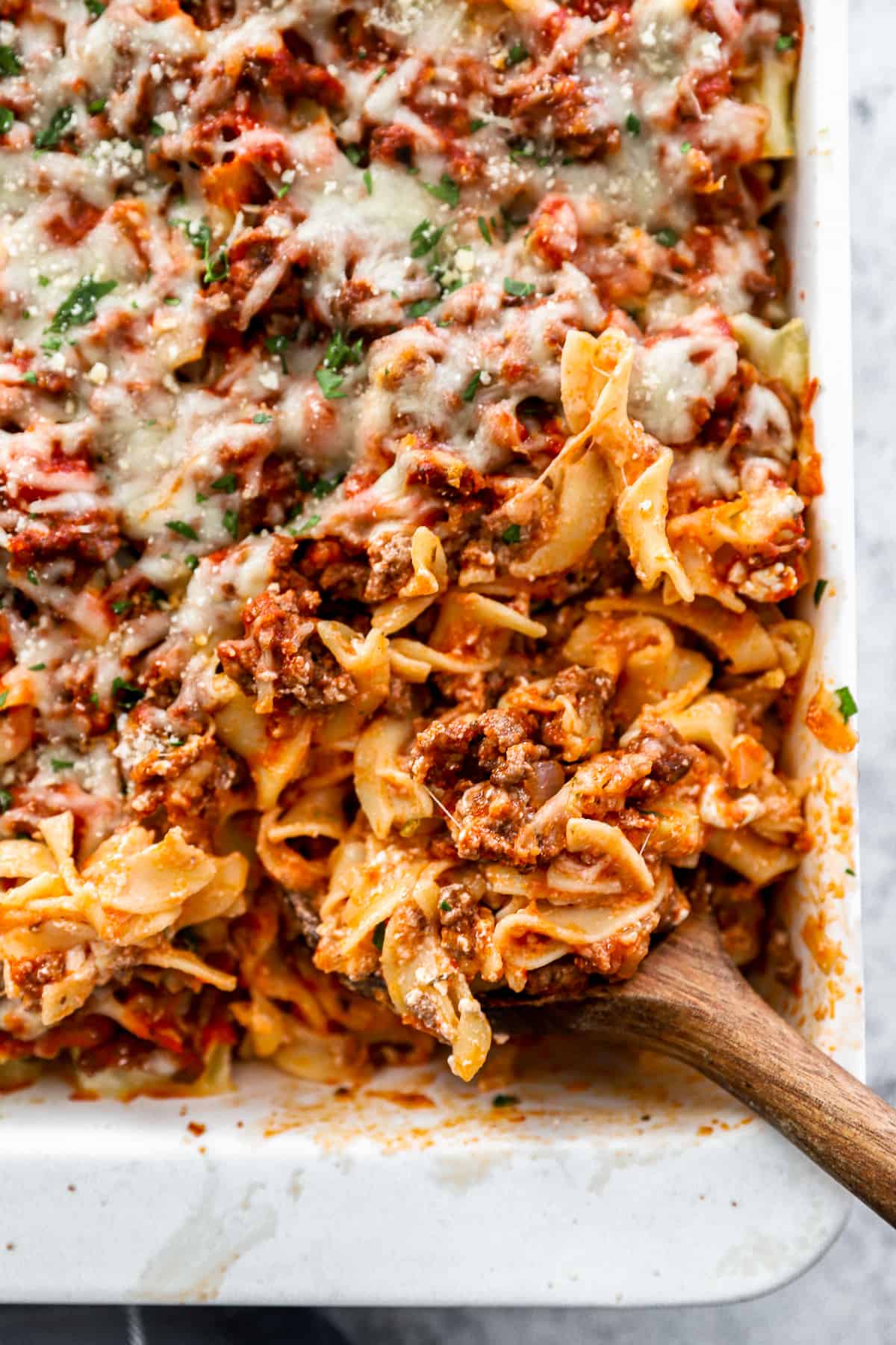 three-quarters view of the lower right corner of a sour cream noodle casserole with a wooden spoon.