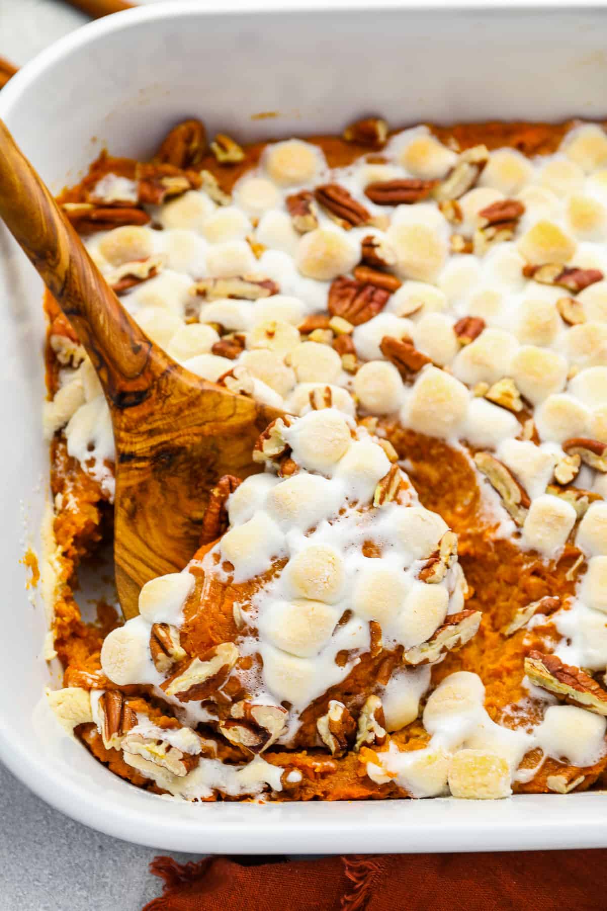 a wooden spoon scooping sweet potato casserole from a white rectangular baking dish.